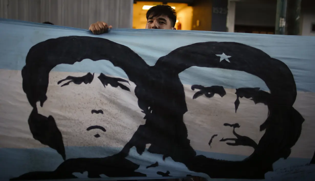 Penggemar berdiri di belakang spanduk bergambar Diego Maradona dan revolusioner Marxis Ernesto "Che" Guevara, di luar Clinica Olivos, tempat legendaris sepak bola Argentina itu akan operasi, di Buenos Aires, Selasa (3/11/2020). Maradona mengalami pembekuan darah di otak. (AP Photo/Natacha Pisarenko)