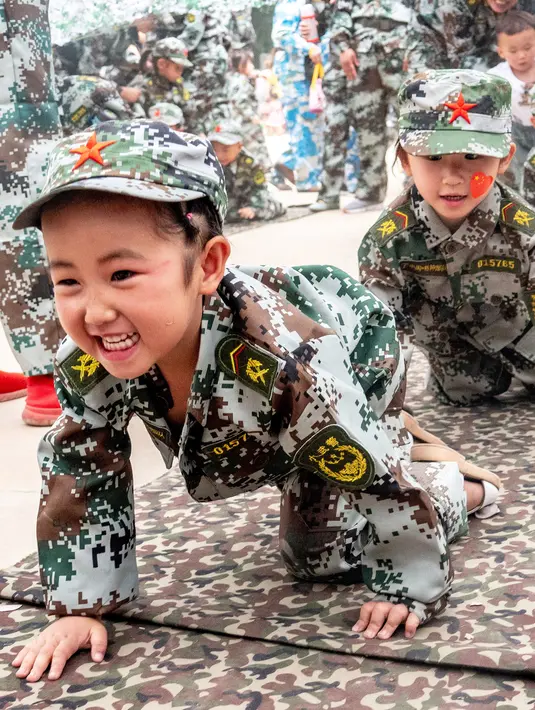 Ekspresi anak-anak saat merangkak dalam mengikuti simulasi latihan militer di sebuah taman kanak-kanak di provinsi Henan, China (30/5). (AFP)