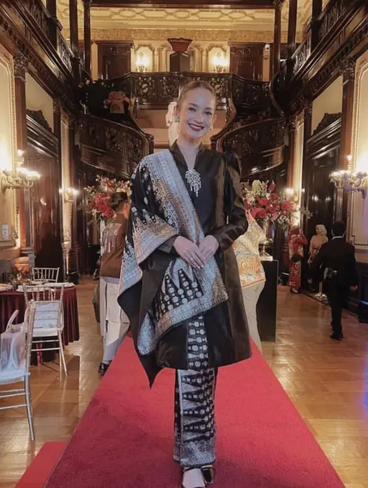 Enzy Storia tampil dengan kebaya hitam panjang satin dipadukan bros dan selendang dan kain bawahan dengan motif yang serasi. [@enzystoria]