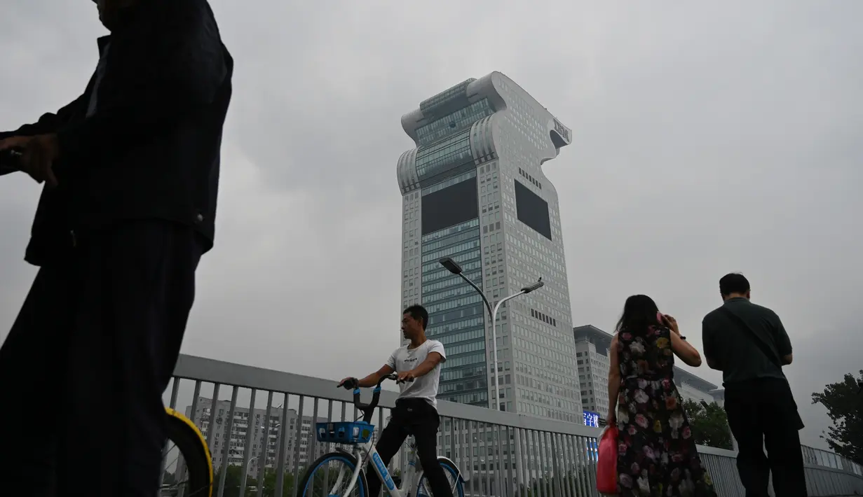 Orang-orang melewati gedung pencakar langit Pangu Plaza di seberang Stadion Olimpiade Bird's Nest, Beijing, Selasa (20/7/2019). Gedung yang pernah masuk dalam film Transformers: Age of Extinction itu terjual dalam lelang online dengan harga 734 juta USD atau sekitar Rp10,5 triliun. (GREG BAKER/AFP)