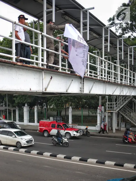 Petugas Satpol PP menertibkan alat peraga kampanye (APK) di jembatan penyeberangan orang (JPO) kawasan Gambir, Jakarta, Sabtu  (22/12). Penertiban itu dilakukan karena melanggar aturan pemasangan dari komisi pemilihan umum. (Liputan6.com/Faizal Fanani)