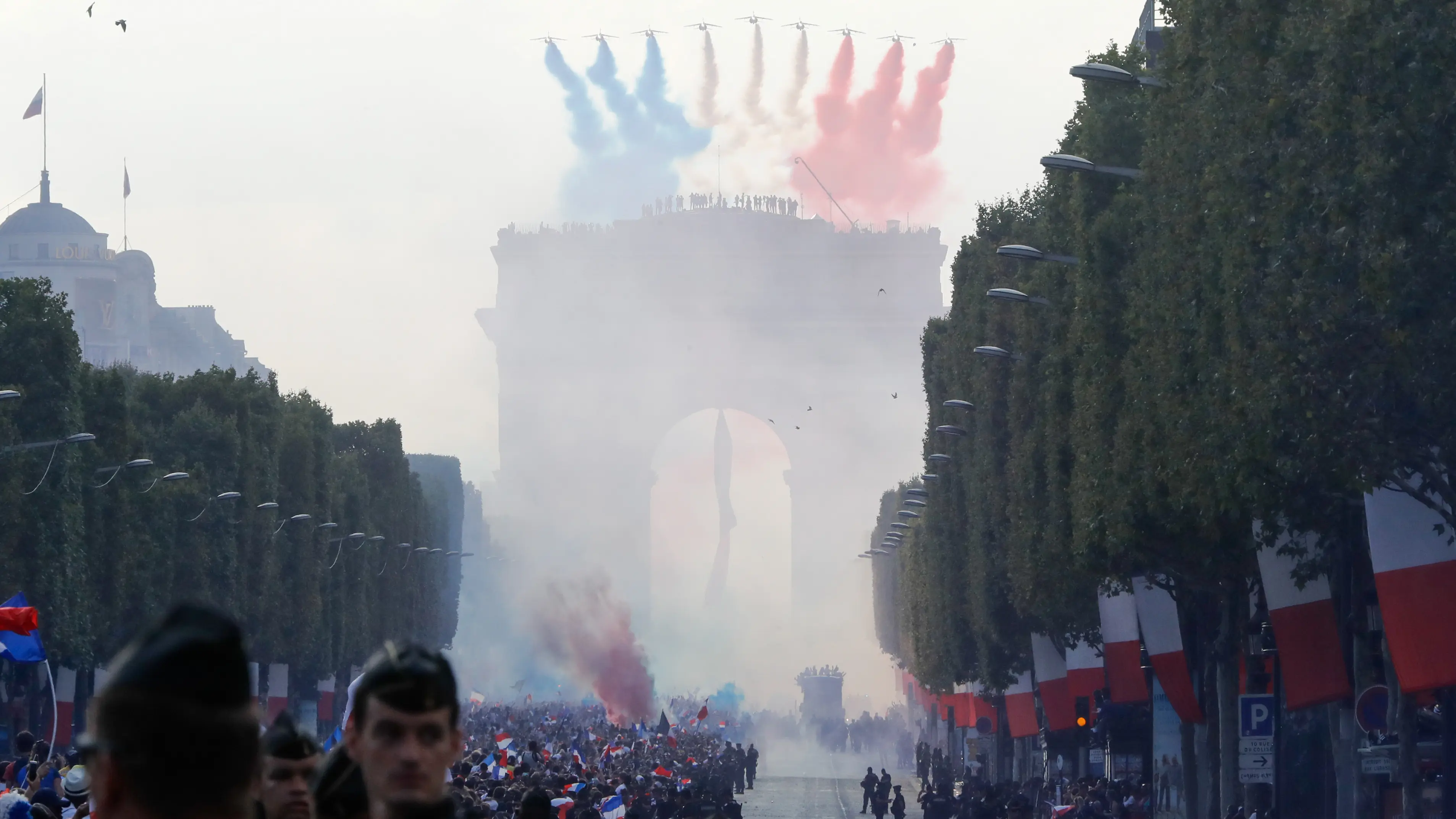 Peswat tempur melepaskan asap berwarna bendera Prancis menyambut kedatangan Les Bleus di Arch of Triumph, Paris, (16/7/2018). Parade tersebut adalah bagian dari perayaan Prancis meraih trofi Piala Dunia 2018. (AFP/Francois Guillot)