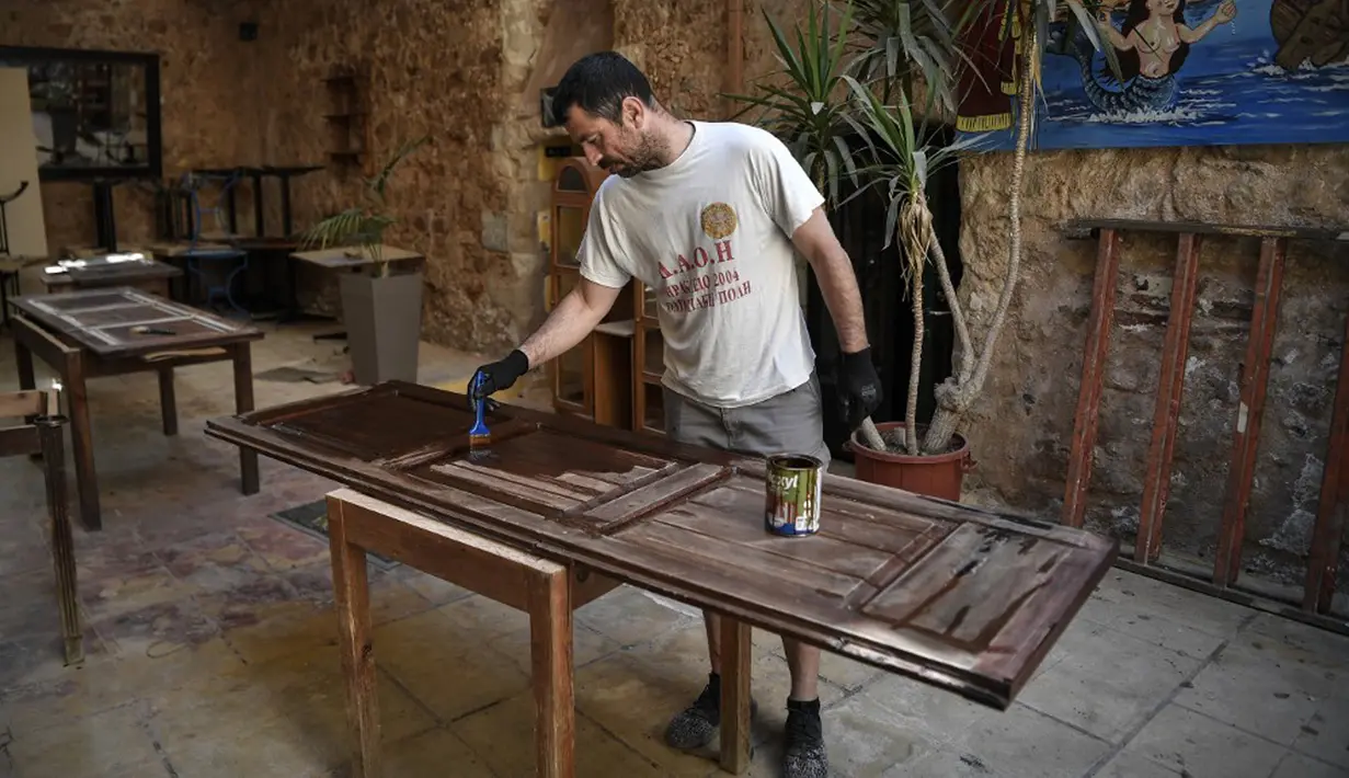 Seorang pekerja memperbaiki pintu di sebuah restoran di Kota Tua Chania (La Canee), barat laut Pulau Kreta, Yunani, Kamis (13/5/2021). Yunani mempermudah langkah-langkah terkait COVID-19 dalam menyambut turis internasional pada 14 Mei. (Louisa GOULIAMAKI/AFP)