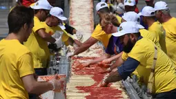 Sejumlah peserta mengoleskan saus tomat saat membuat pizza panjang di jalur Auto Club Speedway, di Fontana, California (10/6). (AFP/Mark Ralston)