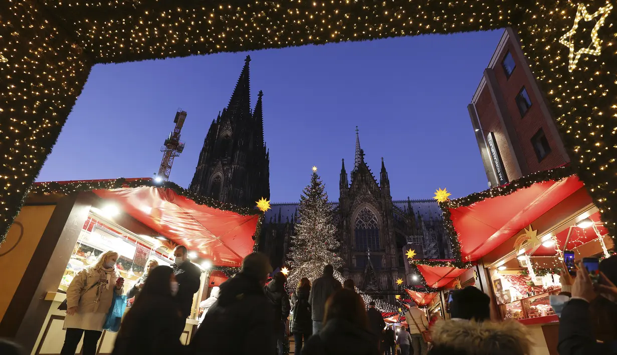 Pengunjung berjalan melalui pasar Natal di Roncalliplatz, Cologne, Jerman, 22 November 2021. Hingga 22 November 2021, angka resmi menunjukkan lebih dari 30.000 kasus baru yang dikonfirmasi di Jerman selama 24 jam terakhir. (Oliver Berg/dpa via AP)