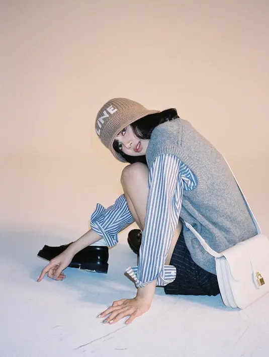 Tampil manis dalam photoshoot brand Celine, Lisa terlihat mengenakan short pants biru navy bermotif garis dengan oversized shirt bermotif garis yang ditumpuknya dengan sweater vest abu-abu. Tampilan preppynya ini disempurnakan dengan oxford shoes hitam dan beanie hat cokelat dari Celine.