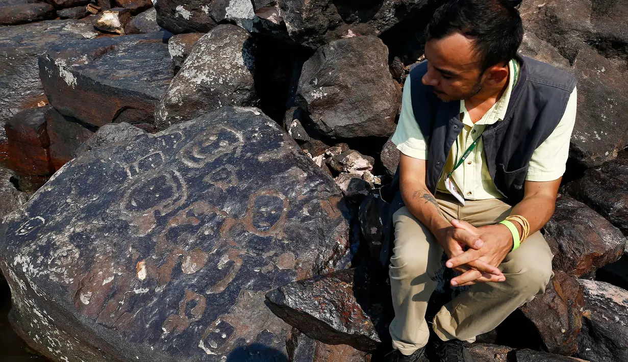 Arkeolog Jaime Oliveira duduk di samping lukisan batu di situs arkeologi Ponta das Lajes, di daerah pedesaan Manaus, Brasil, Sabtu, 28 Oktober 2023. (AP Photo/Edmar Barros)