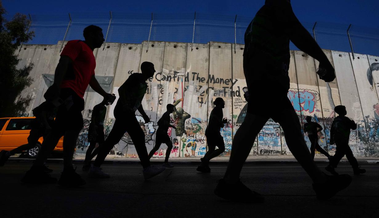 Bukan sekadar ajang olahraga, Maraton Internasional Palestina menjadi medium untuk menyoroti berbagai pembatasan pergerakan yang dialami warga Palestina di bawah pendudukan Israel. Tampak dalam foto, para pelari melewati tembok pemisah Israel saat mereka berkompetisi dalam Maraton Palestina di kota Betlehem, Tepi Barat, Jumat 8 Mei 2026. (AP Photo/Mahmoud Illean)