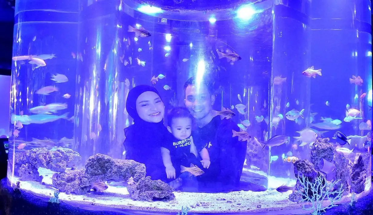 Dalam foto ini, Nathalie Holscher dan Fariz Utama memanfaatkan aquarium berbentuk tabung raksasa transparan yang merefleksikan keduanya bersama baby Adzam. Membiaskan cahaya ungu kebiruan, ketiganya asyik menikmati sejumlah ikan yang berenang di dalam tabung kaca. Hubungan baby Adzam dan Fariz Utama tampak hangat sekaligus dekat. (Foto: Dok. Instagram @farizutama30)