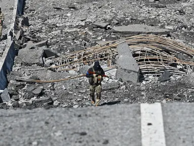 Seorang prajurit Ukraina berjalan melintasi jembatan yang hancur di kota Borodianka, barat laut Kiev pada 4 April 2022. Saat pasukan Rusia mundur, kota kecil Borodianka, 50 km barat laut Kiev, menjadi reruntuhan. (Sergei SUPINSKY / AFP)