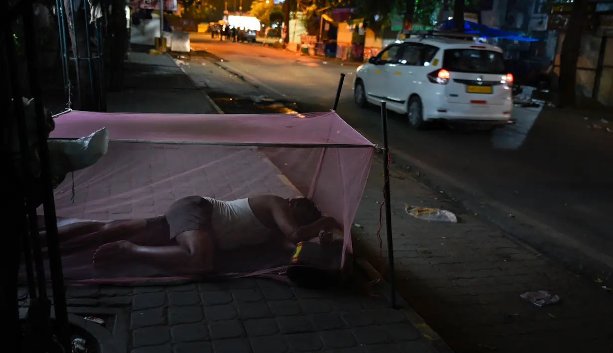 Seorang pria menggunakan jaring antinyamuk saat tidur di trotoar di New Delhi, India, Rabu (17/10). Sekitar 800 juta warga India hidup dalam kemiskinan. (AP Photo / R S Iyer)