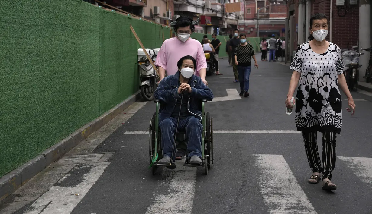 <p>Seorang pria mendorong yang lain di kursi roda dekat penghalang di sekitar komunitas di Shanghai (2/6/2022). Lalu lintas, pejalan kaki dan pelari muncul kembali di jalan-jalan Shanghai ketika kota terbesar di China mulai kembali normal di tengah pelonggaran penguncian COVID-19 dua bulan yang ketat atas penerapannya. (AP Photo/Ng Han Guan)</p>
