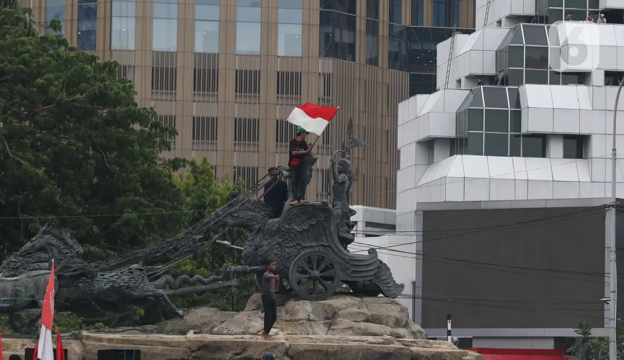 Massa aksi demo tolak omnibus law UU Cipta Kerja naik ke atas patung arjuna wiwaha mengibarkan bendera merah putih di Jalan Medan Merdeka Barat, Jakarta Pusat, Selasa (20/10/2020). Aksi mereka lantas disambut meriah oleh para massa yang masih bertahan. (Liputan6.com/Herman Zakharia)