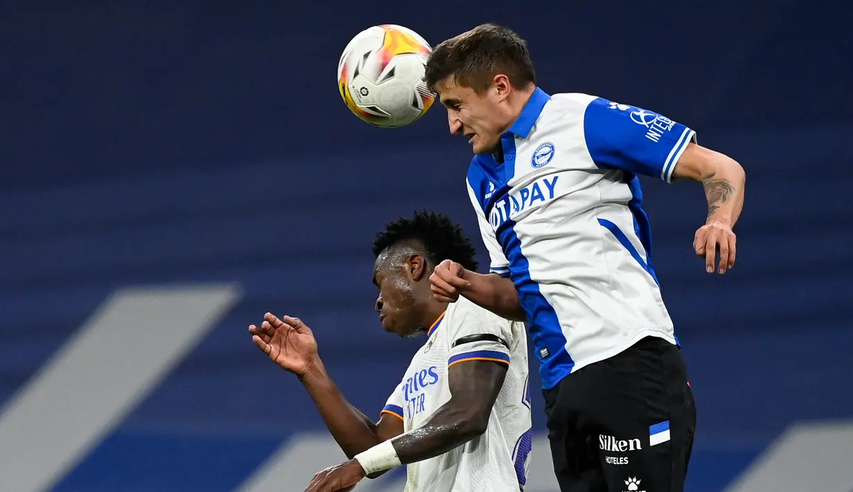 Bek Deportivo Alaves Nahuel Tenaglia berebut bola dengan penyerang Real Madrid Vinicius Junior pada pekan ke-25 La Liga Spanyol di Santiago Bernabeu, Minggu (20/2/2022) dinihari WIB. Real Madrid menang meyakinkan dengan skor 3-0. (OSCAR DEL POZO / AFP)