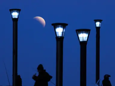 Sejumlah pria berdiri di bawah lampu jalan ketika fenomena gerhana bulan sebagian (parsial) di Buenos Aires, Argentina, Selasa (16/7/2019). Gerhana bulan parsial ini bisa diamati dari Amerika Selatan, Eropa, Afrika, Asia dan Australia. (AP Photo/Natacha Pisarenko)