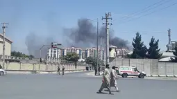 Warga berjalan ketika kepulan asap terlihat setelah ledakan besar di Kabul, Afghanistan, Senin (1/7/2019). Ledakan besar menyebabkan puluhan orang dilarikan ke rumah sakit, baik akibat terkena puing bangunan maupun asap tebal, demikian sebagaimana dikutip dari Al Jazeera pada Senin (1/7/2019). (AFP