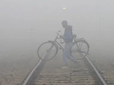 Keluarga menyebrangi jalur kereta api saat kabut tebal di Jalandhar (25/12). India Utara dilanda kabut pagi yang pekat dalam beberapa hari terakhir saat suhu dingin dan kondisi angin rendah turun di wilayah tersebut. (AFP Photo/Shammi Mehra)