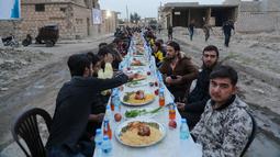 Warga Suriah berkumpul di daerah yang rusak berat untuk berbuka puasa di Tadef, dekat kota perbatasan al-Bab, yang dikendalikan pemberontak yang didukung Turki di Suriah (18/4/2022). Buka puasa ini diselenggarakan oleh sebuah LSM berkoordinasi dengan berbagai faksi lokal. (AFP/Bakr Alkasem)