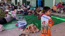 Seorang anak laki-laki mengenakan kaus bergambar tentara berjalan melewati pengungsi lain yang beristirahat di kamp sementara di provinsi Banteay Meanchey pada Sabtu 13 Desember 2025, di tengah bentrokan di sepanjang perbatasan Kamboja-Thailand. Ketegangan di perbatasan Kamboja-Thailand kembali mencapai titik kritis. (Suy Se/AFP)