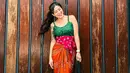 Untuk kamu yang gemar bermain warna, bisa tiru gaya Awkarin satu ini. Padukan tanktop batik hijau, dengan rok lilit oranye dan obi belt merah. [Instagram/narinkovilda]