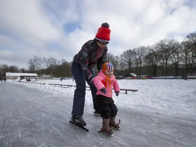 Seorang ibu mengajari putrinya berseluncur di gelanggang es di Doorn, Belanda, Selasa (9/2/2021). Dengan perkiraan suhu beku selama lebih dari seminggu di Belanda, demam es melanda Negeri Kincir Angin tersebut. (AP Photo/Peter Dejong)