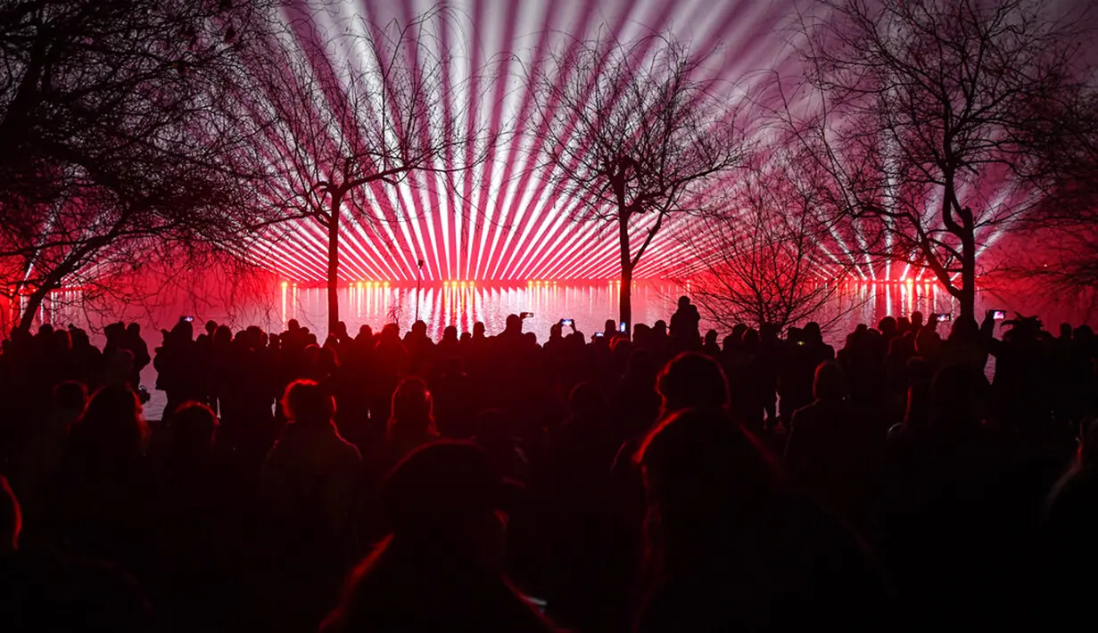 Orang-orang menonton pertunjukan laser saat perayaan Tahun Baru di Bucharest, Rumania, Sabtu (1/1/2022). Ribuan orang berkumpul di tepi danau untuk menghadiri konser dan menonton kembang api serta pertunjukan laser pada perayaan Tahun Baru. (AP Photo/Andreea Alexandru)
