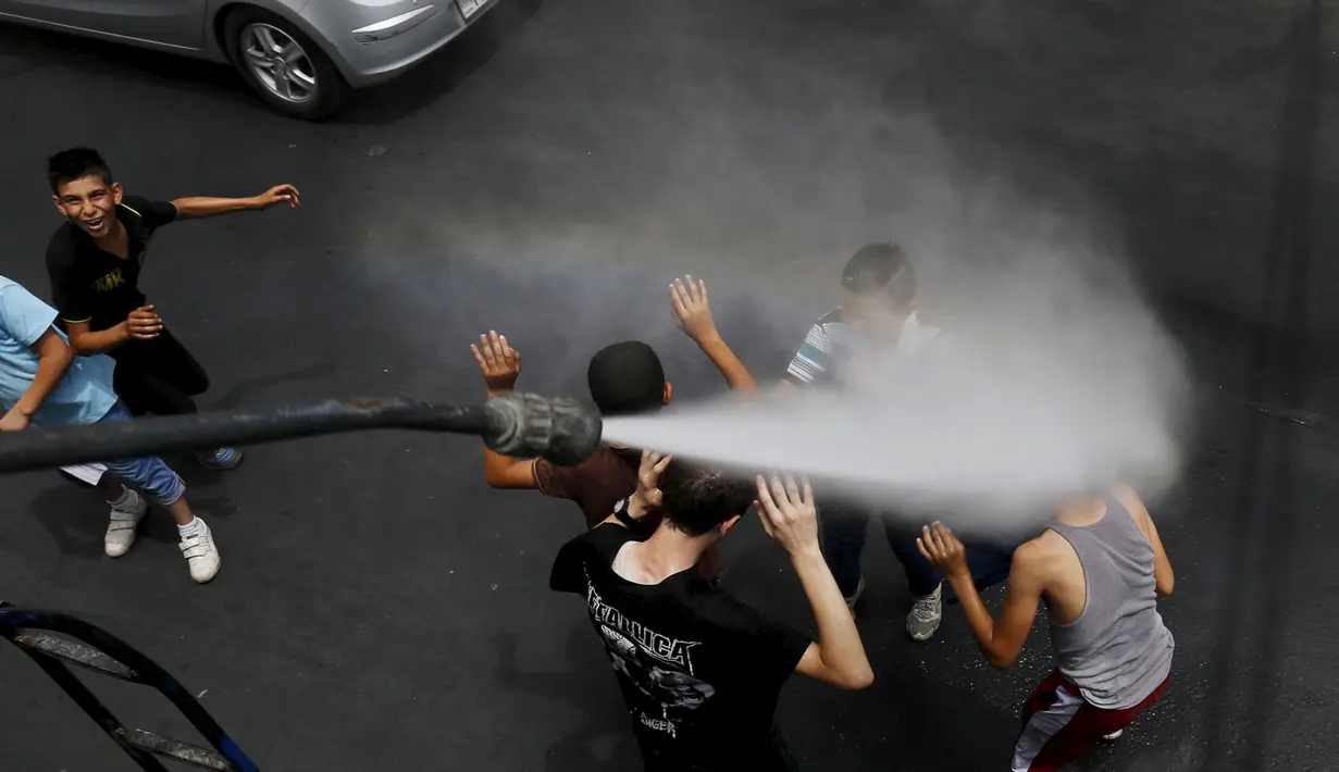 Personel dinas Kota Amman menyemprot sejumlah anak dengan sprinkler air untuk mengurangi efek dari gelombang panas di Yordania, Senin(3/8/2015). (REUTERS/Muhammad Hamed)