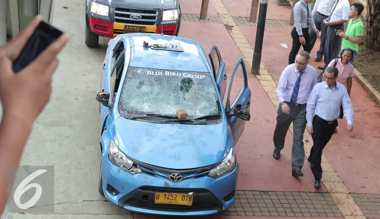 Sejumlah pekerja melihat kondisi mobil taksi yang hancur akibat dirusak oleh ojek online di Jakarta, Selasa (22/3). Kedua transportasi tersebut saling serang dan menswiping satu sama lain. (Liputan6.com/Angga Yuniar)