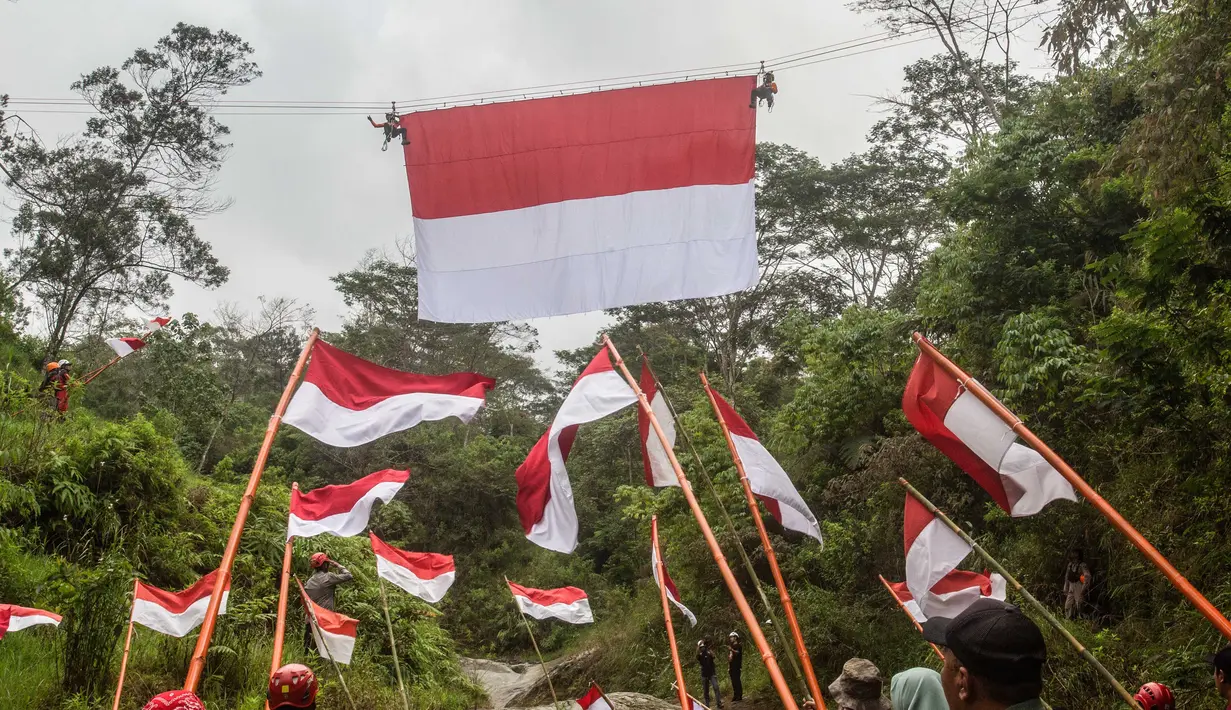 Personel Badan Pencarian dan Pertolongan Nasional (Basarnas) memasang bendera Merah Putih yang digantung pada tali yang membentang di atas sungai di Watu Kemloso, Yogyakarta, pada 13 Agustus 2025, menjelang peringatan ke-80 Hari Kemerdekaan Indonesia. (DEVI RAHMAN/AFP)