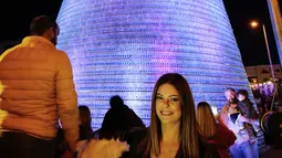 Caroline Chaptini berpose di depan Pohon Natal raksasa yang terbuat dari botol plastik di kota Chekka, Lebanon, 15 Desember 2019. Tujuan proyek ini adalah untuk memecahkan Guinness World Record sebelumnya, yakni pohon Natal yang dibangun dari 98.000 botol di Meksiko. (Ibrahim CHALHOUB/AFP)