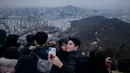 Pasangan berselfie di sudut pandang yang menghadap ke cakrawala kota untuk menyaksikan matahari terbit pertama tahun baru, meskipun dalam kondisi mendung, di Seoul, Korea Selatan (1/1/2020). (AFP/Ed Jones)