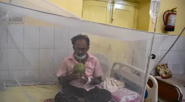 Seorang pasien minum air kelapa saat dia duduk di bawah kelambu di bangsal demam berdarah sebuah rumah sakit pemerintah di Allahabad, India (30/8/2021). (AFP/Sanjay Kanojia)
