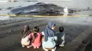 Pemeriksaan menyeluruh (nekropsi) untuk memastikan penyebab kematian, apakah karena sakit, faktor usia, atau tertelan sampah laut masih dilakukan. Tampak dalam foto, anak-anak berkumpul di dekat bangkai paus sperma yang terdampar, sementara petugas konservasi masih menyelidiki penyebab kematiannya, menjelang rencana penguburan di salah satu tempat di pantai Banjar Anyar Sari, Desa Nusasari, Kecamatan Melaya, Jembrana, Bali, pada Rabu 6 Mei 2026. (Lana Priatna/AFP)