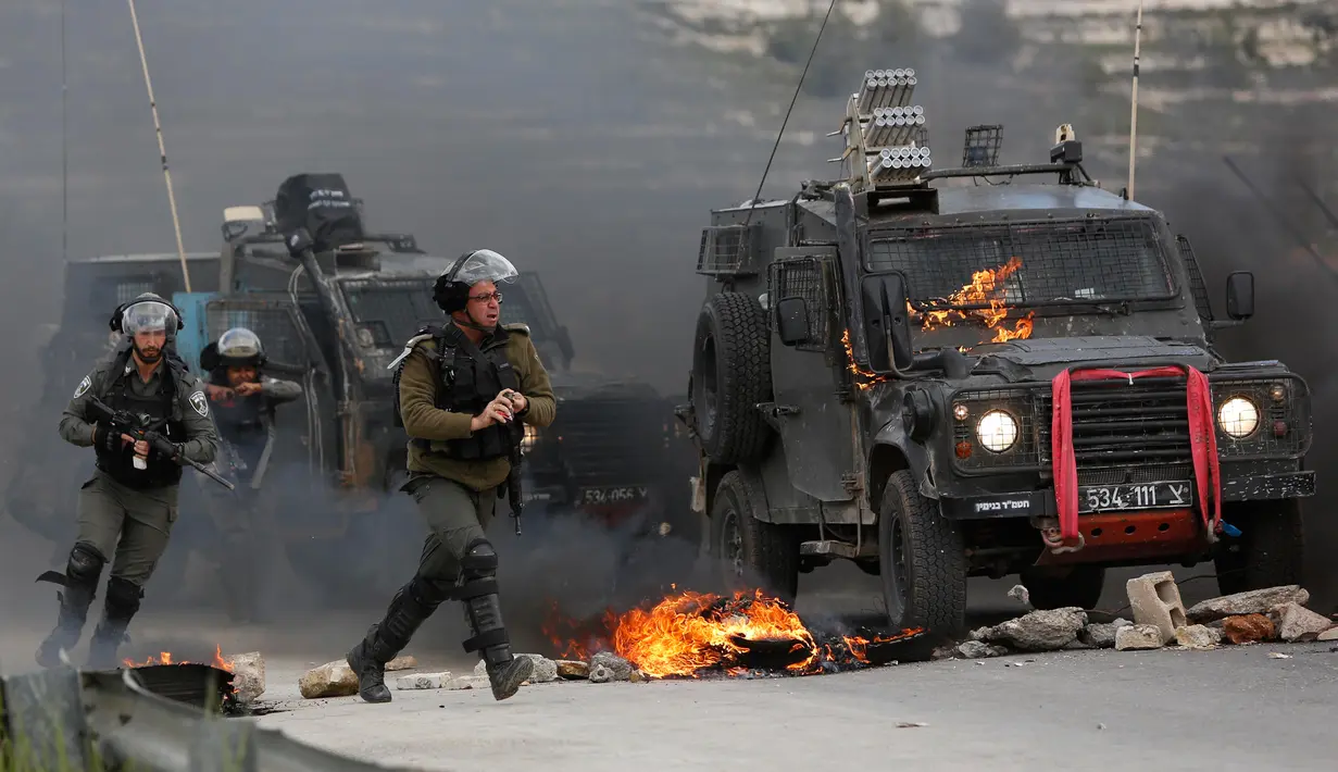 Tentara Israel mengejar pengunjuk rasa saat kendaraan militer mereka terbakar oleh lemparan bom molotov warga Palestina di pinggiran Kota Ramallah, Tepi Barat, Rabu (27/3). Bentrokan ini sebagai bentuk protes terhadap tahanan Palestina yang berada di Israel. (AP Photo/Majdi Mohammed)