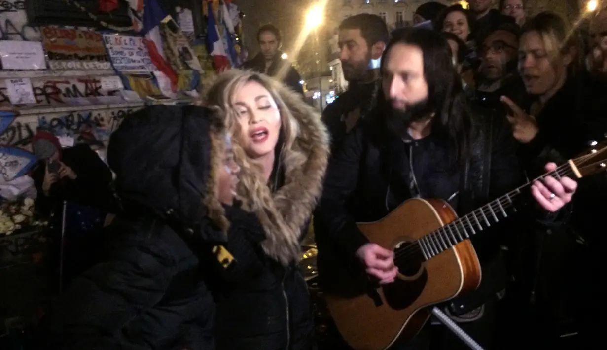 Penyanyi Madonna (tengah) bernyanyi di samping gitarisnya Monte Pittman (tengah kanan) dan anaknya David Banda (kiri) di place de la Republique di Paris untuk mengenang korban serangan teror 13 November di Paris, Kamis (10/12/2015). (JULES MAHE/AFP)