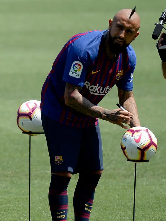 Pemain baru Barcelona, Arturo Vidal menandatangani bola selama presentasi dirinya di stadion Camp Nou, Spanyol, (6/8). Vidal resmi diboyong Barcelona dengan kontrak selama tiga tahun. (AFP Photo/Josep Lago)