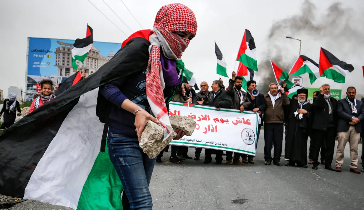 Seorang wanita Palestina membawa batu selama bentrokan dengan tentara Israel dalam demonstrasi untuk memperingati Hari Tanah di Tepi Barat, Sabtu (30/3).(Photo by ABBAS MOMANI/AFP)