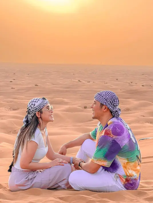 Kali ini keduanya berpose di padang pasir di Dubai. Via Vallen tampil santai dengan atasan lengan pendek berwarna putih dan celana panjang berwarna ungu muda, serta penutup kepala dan kacamata hitam. Sedangkan suaminya tampil dengan tie-dye shirt dan celana panjang berwarna putih, lengkap dengan penutup kepala. Foto: Instagram.
