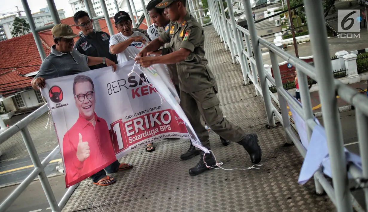 Petugas Satpol PP mencopot alat peraga kampanye (APK) berupa spanduk caleg di JPO kawasan Gambir, Jakarta, Sabtu  (22/12). PenertiBan spanduk APK dilakukan karena melanggar aturan pemasangan dari komisi pemilihan umum. (Liputan6.com/Faizal Fanani)