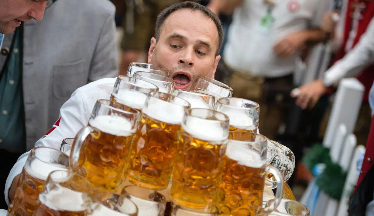 Oliver Struempfel membawa gelas bir sambil berjalan untuk memecahkan rekor pada festival tradisional Gillamoos di Abensberg, Jerman, Minggu (3/9). Ia berhasil menyusun 29 gelas dan membawanya dengan dua tangan dalam sekali jalan (Matthias Balk/dpa via AP)