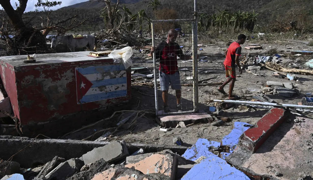 Seorang pria memegang gerbang rumah yang rusak akibat Badai Melissa di desa Boca de Dos Rios, provinsi Santiago de Cuba, Kuba, pada Kamis 30 Oktober 2025. Pada Rabu (29/10/2025), pagi waktu setempat, sejumlah pejabat melaporkan beberapa rumah runtuh, jalan pegunungan terblokir, dan atap bangunan beterbangan akibat terjangan Badai Melissa. 
(YAMIL LAGE/AFP)