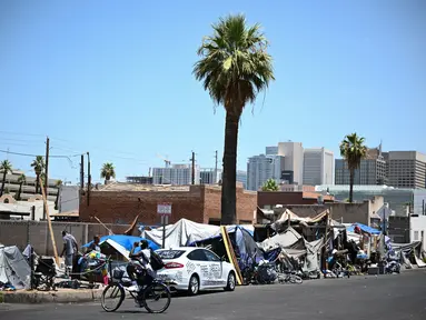 Seorang pengendara sepeda melewati orang-orang yang sedang berkemah di "The Zone", perkemahan tunawisma yang luas tempat ratusan orang tinggal, selama rekor gelombang panas di Phoenix, Arizona, pada 18 Juli 2023. (Patrick T. Fallon / AFP)