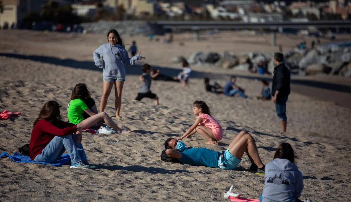 Orang-orang bersantai di pantai di Badalona, dekat Barcelona, Spanyol, Selasa, (28/4/2020). Lockdown untuk memerangi penyebaran virus corona terus berlanjut di Spanyol. (AP Photo/Emilio Morenatti)