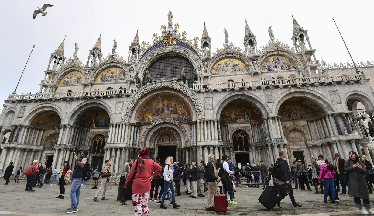 Wisatawan berjalan melintasi Lapangan Santo Markus dengan latar Basilika Santo Markus di Venesia (4/11/2019). Basilika Santo Markus adalah gereja di Venesia paling terkenal dan salah satu contoh yang paling terkenal dari arsitektur Bizantium. (AFP Photo/Miguel Medina)