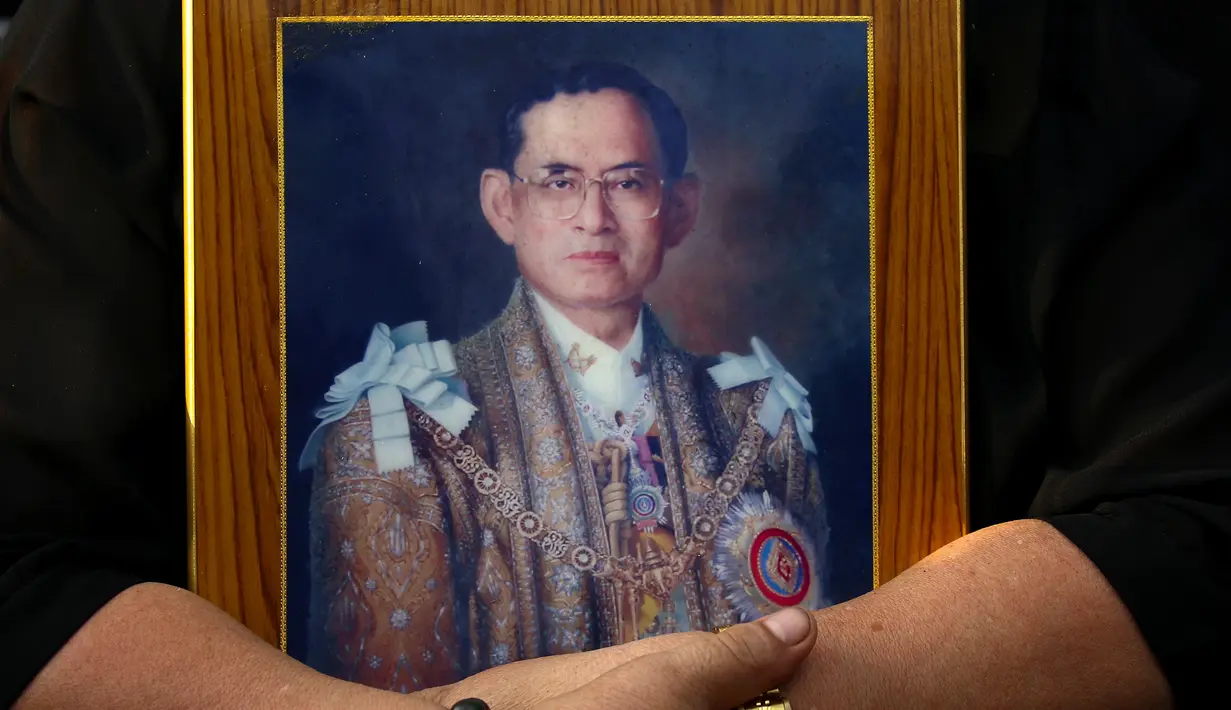 Seorang warga memegang foto Raja Bhumibol Adulyadej jelang pemindahan jenazah ke Grand Palace, Bangkok, Thailand, Jumat (14/10). (REUTERS / Athit Perawongmetha)