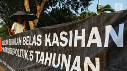 Aktivis JSKK membentangkan spanduk saat menggelar aksi Kamisan ke-589 di depan Istana Merdeka, Jakarta, Kamis (20/6/2019). Dalam aksinya, JSKK meminta Presiden Joko Widodo memegang teguh komitmen untuk menyelesaikan pelanggaran HAM berat masa lalu. (Liputan6.com/Johan Tallo)