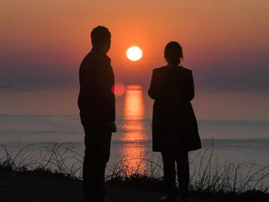 Pasangan melihat matahari terbenam di Cap Frehel, di Plevenon, Prancis barat (26/2). Cap Fréhel adalah semenanjung di Côtes-d'Armor, di Brittany utara, Prancis yang membentang dari Côte d'Émeraude ke Golfe de Saint-Malo. (AFP Photo/Loic Venance)