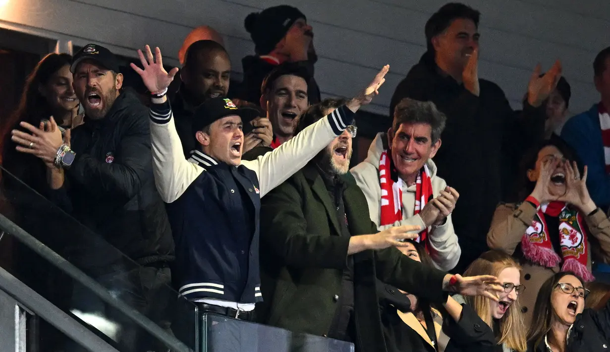 Aktor Hollywood, Ryan Reynolds (kiri) dan pemilik klub Wrexham, Rob McElhenney merayakan kemenangan timnya saat laga English National League antara Wrexham melawan Boreham Wood di Racecourse Ground Stadium, Wrexham, Wales, Sabtu (22/04/2023). Wrexham menang dengan skor 3-1 dan berhasil promosi ke Liga Dua Inggris. (AFP/Oli Scarff)