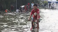 Seorang anak bermain sepeda di genangan air akibat banjir rob di kawasan pintu masuk Pelabuhan Nizam Zachman, Muara Baru, Jakarta, Jumat (5/6/2020). Banjir rob di Pelabuhan Muara Baru tersebut terjadi akibat cuaca ekstrem serta pasang air laut. (Liputan6.com/Helmi Fithriansyah)