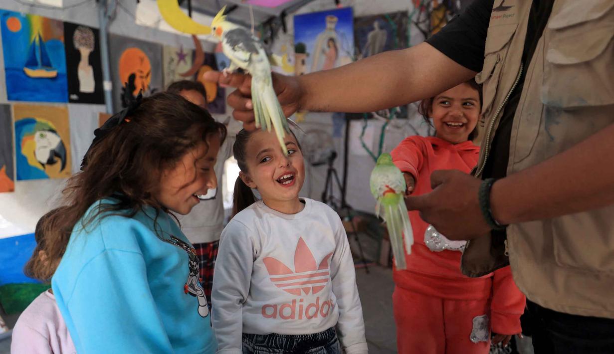 Untuk diketahui, di Gaza, burung sering menjadi simbol harapan dan ketahanan dalam karya seni lokal. Tampak dalam foto, anak-anak pengungsi Palestina mengikuti sesi konseling psikologis di sebuah studio seni yang menggunakan hewan peliharaan dan burung di daerah Al-Zawaida, Jalur Gaza Tengah, pada Selasa 21 April 2026. (Eyad Baba/AFP)